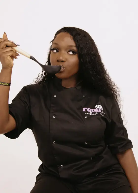 Serena tasting food from a fork in her branded chef jacket